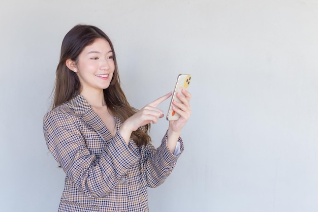 Femme professionnelle asiatique aux cheveux longs noirs portant un costume à carreaux avec un travail réussi à l'aide d'un smartphone