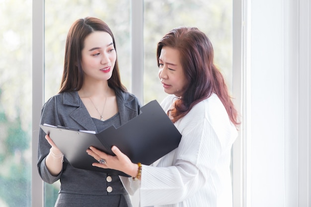 Photo une femme professionnelle asiatique s'entretient avec sa patronne pour la consulter sur le travail dans un document de fichier entre ses mains sur le lieu de travail.