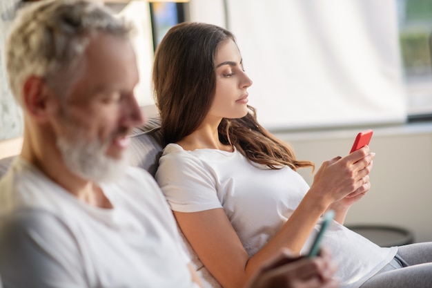 Femme de profil avec de longs cheveux noirs et un homme aux cheveux gris regardant de près dans le smartphone