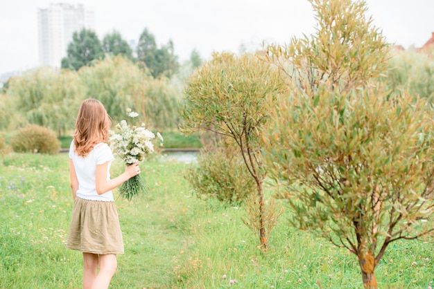 Femme profitant de la vie sur le terrain avec des fleurs. Beauté de la nature, ciel nuageux et champ coloré avec des fleurs. Mode de vie en plein air. Concept de liberté. Femme dans le champ de l&#39;été