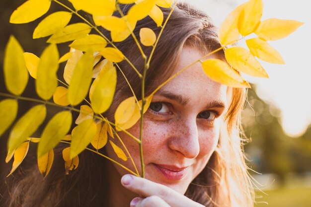 Femme profiter de l'automne dans le parc. Feuille jaune sur le visage féminin, beau portrait saisonnier