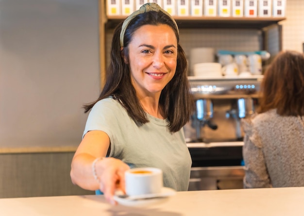 Femme propriétaire de café avec un latte à la main offrant le café au client