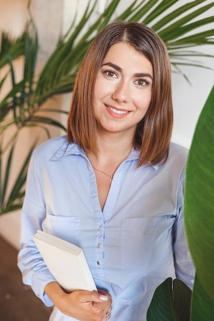 Femme psychologue avec livre au bureau avec des plantes tropicales