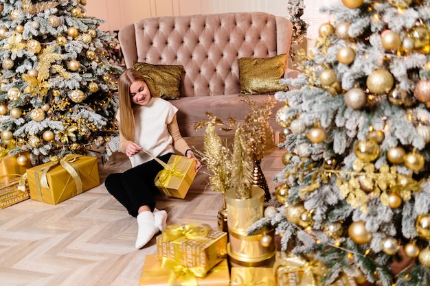 Femme en pull blanc, soirée chaleureuse et cosy dans un intérieur de Noël, sapin de Noël décoré de lumières, guirlande s'éclairant à l'intérieur. Mise au point douce