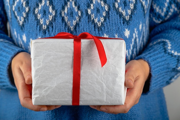 Femme en pull bleu tenant un cadeau de Noël minimaliste blanc