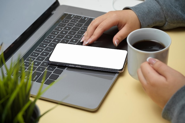 Femme en pull gris en sirotant un café noir et en utilisant un smartphone sur sa table de travail