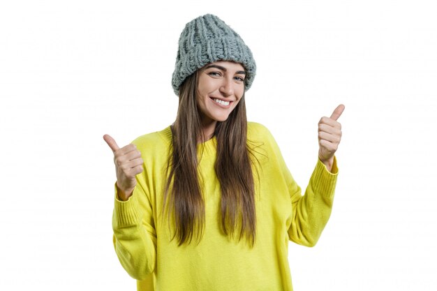 Femme en pull jaune et chapeau gris, montrant des signes ok pouce levé