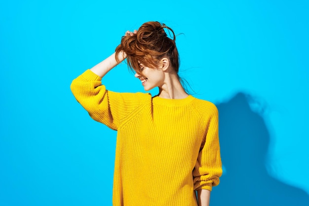 Femme en pull jaune posant une coiffure de mode fond bleu Photo de haute qualité