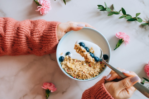 Femme en pull de laine corail mangeant un bol de petit-déjeuner avec muesli et yaourt, baies et noisettes