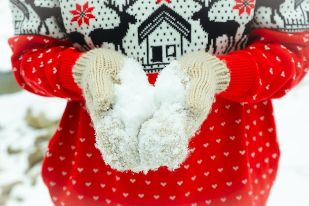 Photo femme en pull et mitaines de noël tient la neige en plein air