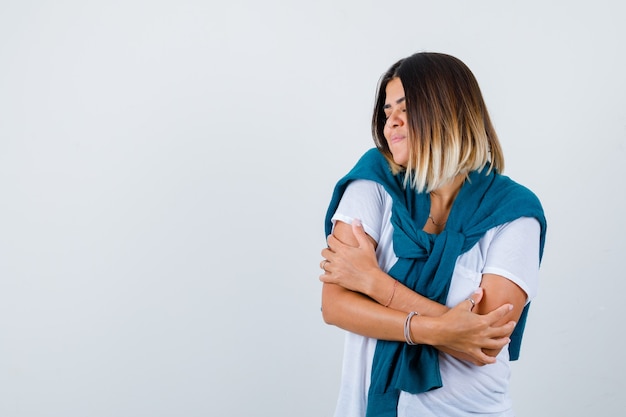 Photo femme avec un pull noué posant tout en se serrant dans ses bras en t-shirt blanc et l'air paisible. vue de face.