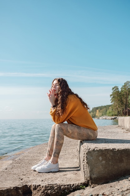 Femme en pull orange assis sur un escalier en pierre sur une plage avec ses yeux fermés, mise au point sélective