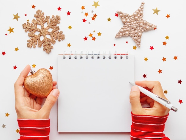 Photo femme en pull rouge écrit ou dessine dans un bloc-notes avec des pages de papier blanc cœur décoratif noël