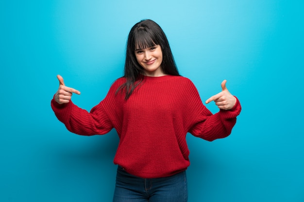 Femme avec un pull rouge sur un mur bleu fier et satisfait