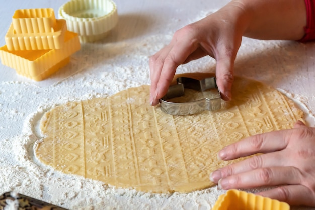 Femme en pull rouge et tablier orange sculpte des biscuits sur la pâte.