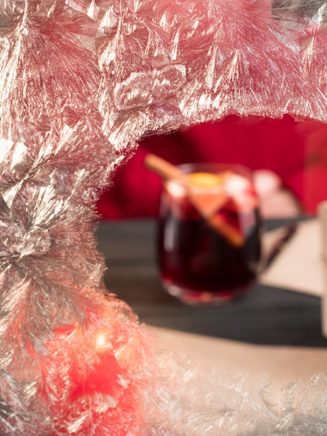 Une femme en pull rouge tient un verre de vin chaud derrière un verre gelé. Vacances de Noël.