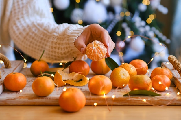 Une femme en pull tricoté fait une composition de Noël pour une ambiance festive, des mandarines et une décoration de sapin derrière. arôme de vacances. Mise au point sélective