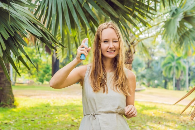 Femme pulvérisant un insectifuge sur la peau à l'extérieur.