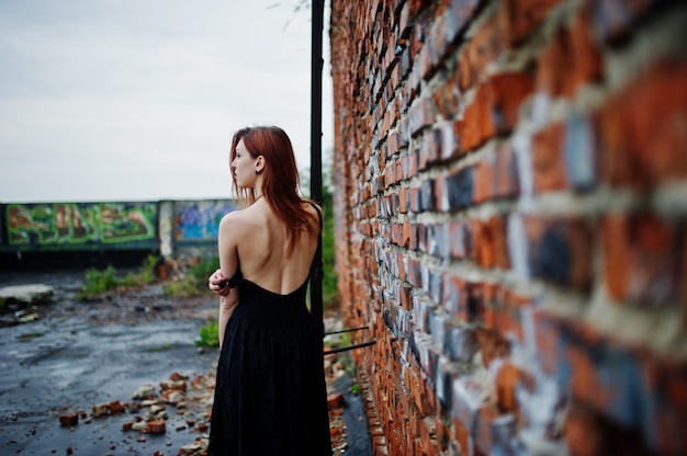 Femme punk aux cheveux rouges porter sur une robe noire sur le toit contre le mur de briques avec échelle de fer.