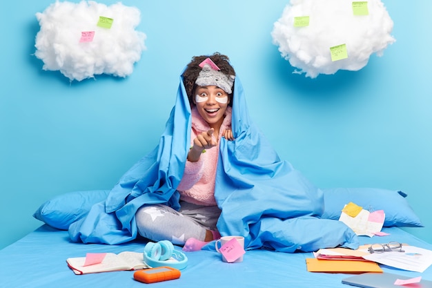 une femme en pyjama avec une grande surprise prépare des poses de projets créatifs à bedroon sur un lit confortable prend des notes sur des autocollants travaille à la maison