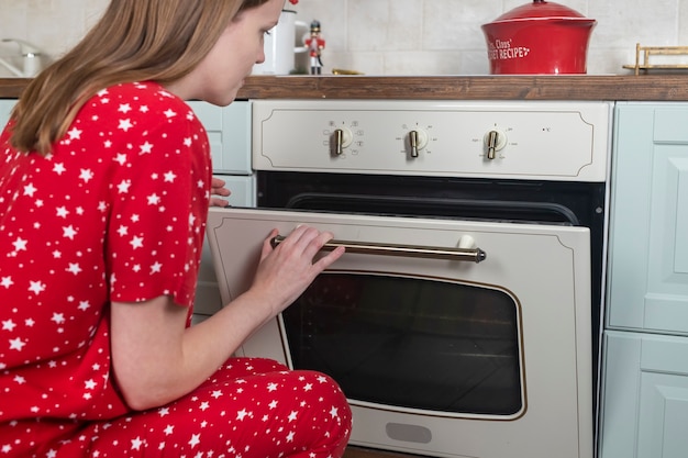 Femme en pyjama ouvrant le four pour cuisiner à la maison