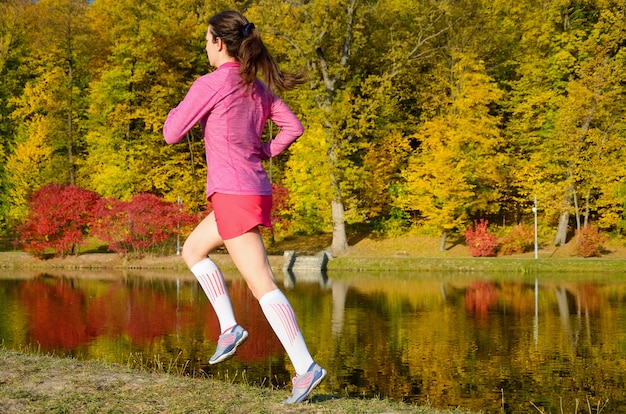 Femme qui court dans le parc en automne, coureur de belle fille jogging en plein air, formation pour le marathon, l'exercice et le concept de remise en forme