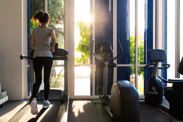 Femme qui court dans la salle de fitness sur appareils d&#39;exercice sur tapis roulant.