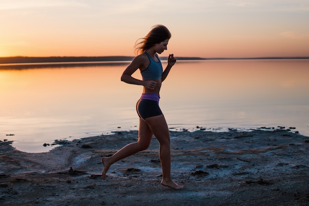 Femme qui court sur la plage au coucher du soleil.