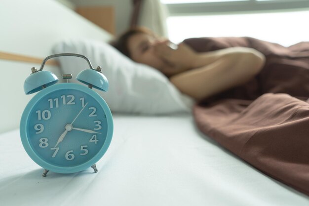 Une femme qui dort sur un lit avec un réveil au premier plan.