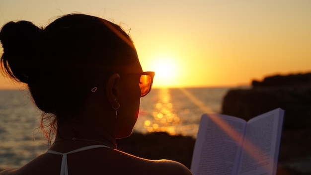 Photo une femme qui lit au coucher du soleil sur la côte rocheuse aime un livre