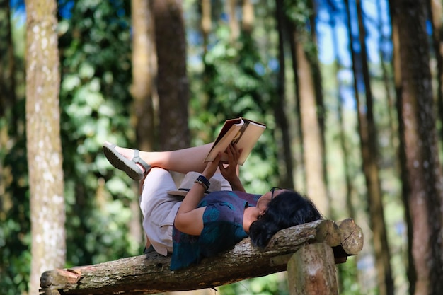 Une femme qui profite de son temps libre allongée sur un banc de bois en train de lire un livre seule dans le parc