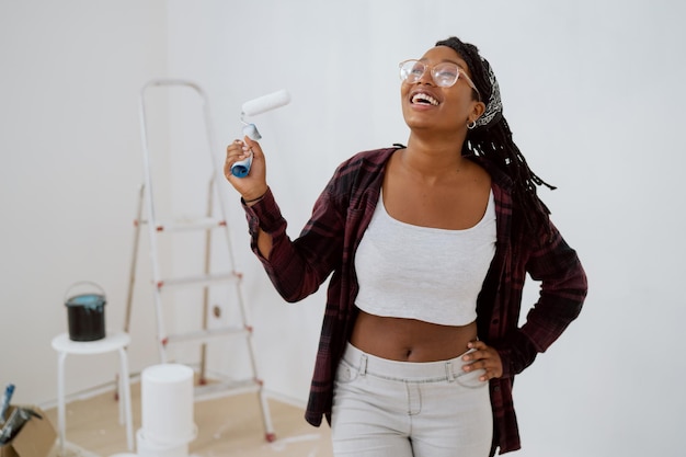 Une femme qui rit avec des lunettes sourit avec des dents enneigées la fille tient un rouleau pour appliquer de la peinture blanche