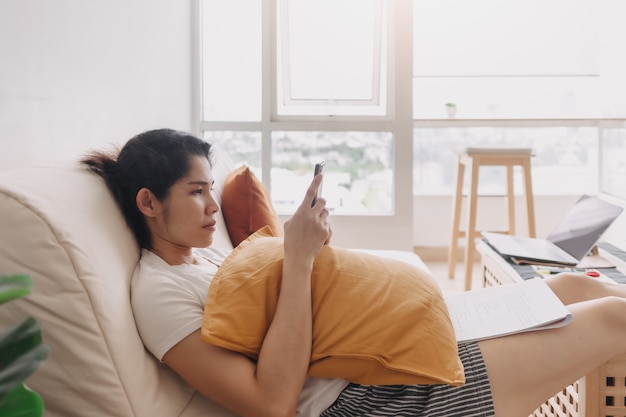 Une femme qui s'ennuie utilise les réseaux sociaux de son smartphone pour tuer le temps dans un appartement