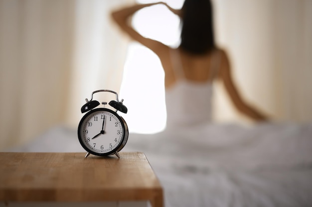 Femme qui s'étire les mains dans son lit après le réveil, éruption solaire. Brunette entrant dans une journée heureuse et détendue après une bonne nuit de sommeil et une vue arrière. Concept d'un nouveau jour et d'un week-end joyeux.