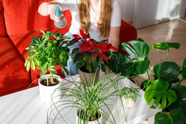 Photo femme qui s'occupe et arrose des plantes d'intérieur à la maison à l'aide d'une bouteille de pulvérisation