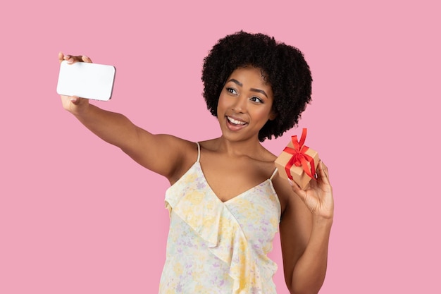 Une femme qui se fait un selfie avec un téléphone et une petite boîte rouge.