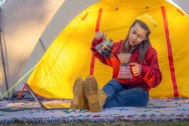 Une femme qui travaille boit un café et travaille avec un carnet de notes informatique entre le camping sous tente
