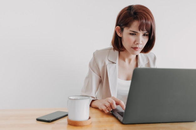 La femme qui travaille utilise un ordinateur portable sur le bureau avec un fond blanc