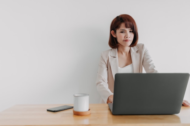 La femme qui travaille utilise un ordinateur portable sur le bureau avec un fond blanc