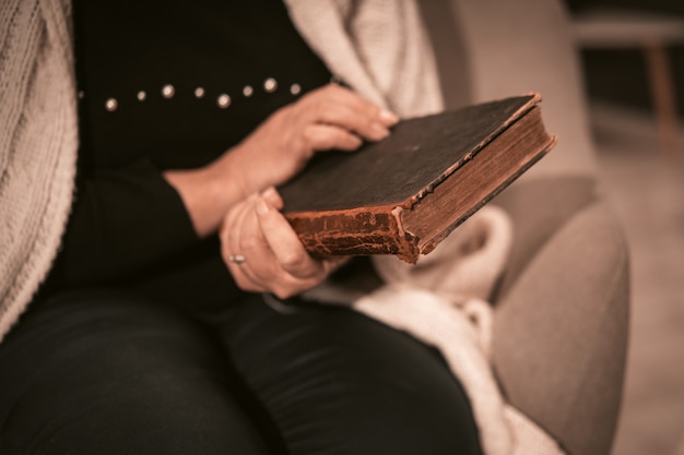 Une femme de race blanche âgée tient un livre ancien dans ses mains