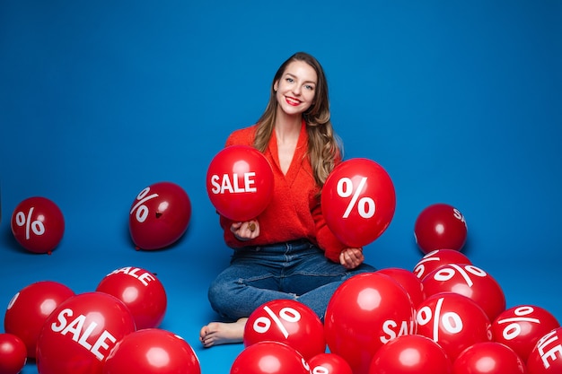 Femme De Race Blanche Avec Une Apparence Attrayante Est Assise Avec Des Ballons Avec Un Pourcentage D'impression, Photo Sur Bleu