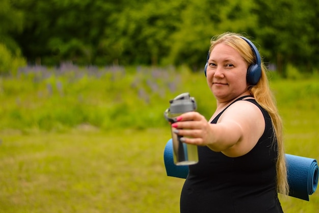 Une femme de race blanche blanche de grande taille dans un casque, un t-shirt noir avec un tapis de yoga dans les mains, marche dans la rue