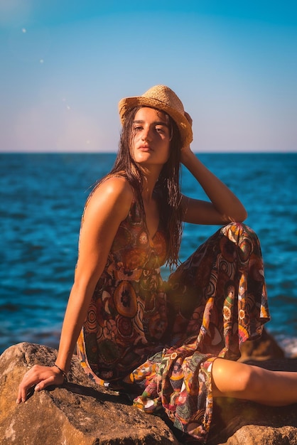 Femme de race blanche avec les cheveux mouillés et une robe à fleurs et un chapeau de paille au bord de la mer