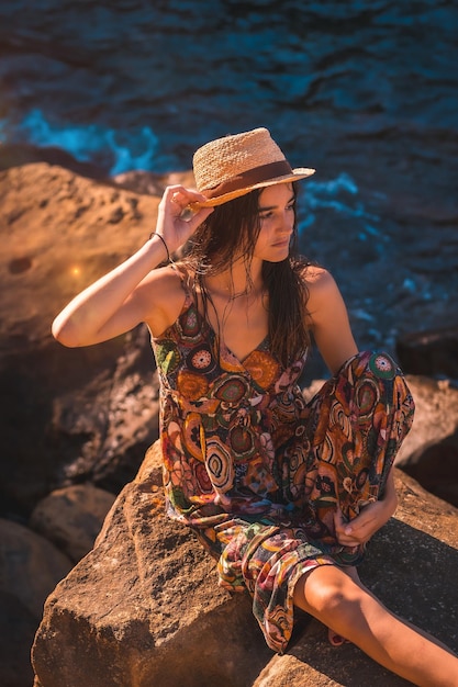 Femme de race blanche avec les cheveux mouillés et une robe à fleurs et un chapeau de paille au bord de la mer