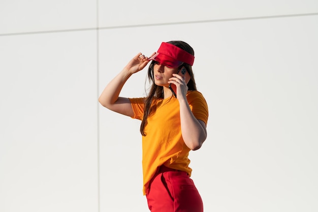 Femme de race blanche élégante dans un t-shirt orange et une casquette rouge parlant au téléphone