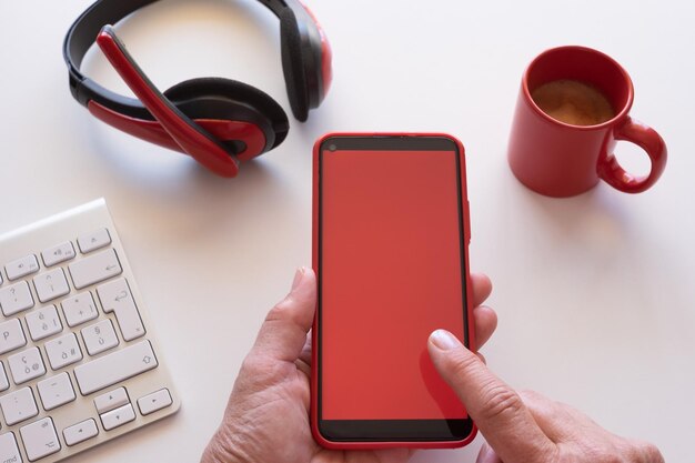 Une femme de race blanche fait une pause avec une tasse de café en utilisant un téléphone avec un écran rouge Un bureau blanc et un casque rouge