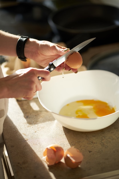 Femme de race blanche ouvrant un œuf pendant la cuisson du petit-déjeuner. Bouchent les mains