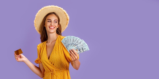 Une femme de race blanche portant un chapeau de paille tenant une carte de crédit et un fan d'argent en dollars isolé sur violet ...