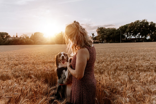 Femme de race blanche senior jouant avec un chien border collie sur un champ de blé. Notion d'amitié