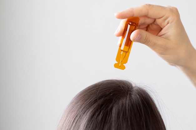 Femme de race blanche tenant une ampoule de vitamines et appliquer sur les cheveux ou la peau en gros plan les cheveux et la peau